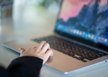 Close-up of a hand using a laptop in a modern office environment, symbolizing remote work.